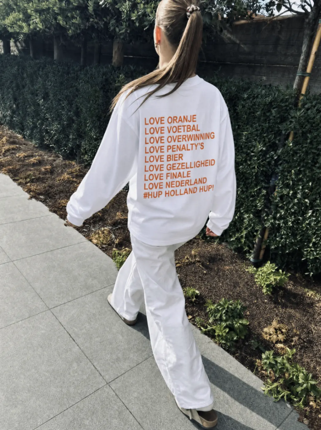 Witte WK longsleeve met oranje backprint tijdens een zonnige wandeling buiten.