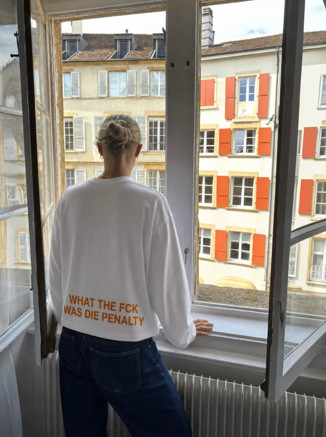 Witte cropped WK longsleeve met oranje quote, gefotografeerd bij een open raam.