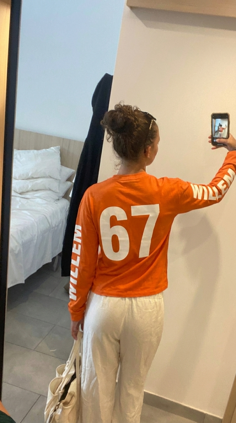 Oranje longsleeve met witte '67' rugprint en 'Willem' op de mouw, gedragen met crèmewitte broek — Koningsdag streetstyle look